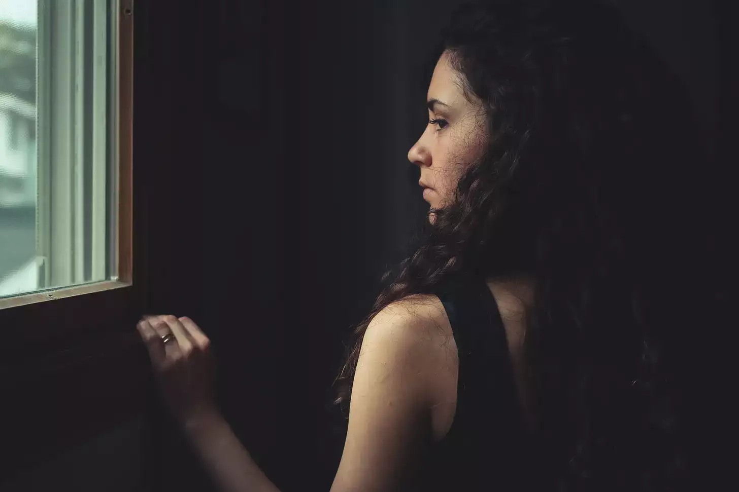 [ Photo of a woman in a dark room, gazing out a window into daylight ]